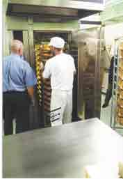 Photo shows an inmate and supervisor checking bread in an industrial oven. 